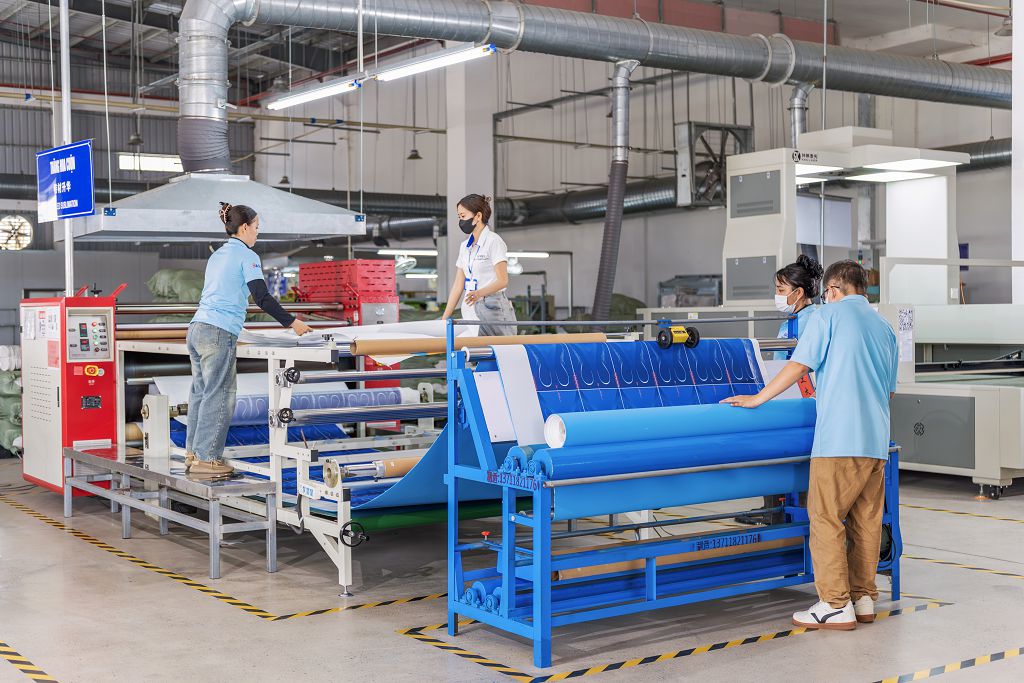 Workers operating a roller heat press to transfer sublimation graphics onto shoe insole cover material.